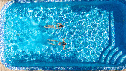 Wall Mural - Active girls in swimming pool water aerial drone view from above, children swim, kids have fun on tropical family vacation, holiday resort concept
