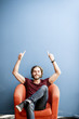 © rh2010 - Portrait of a young caucasian bearded man with long hair showing with hands on the colorful background sitting on the chair. Image with copy space