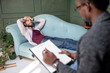 © rh2010 - Young caucasian man visiting an african psychologist lying on the comfortable couch during psychological session in the green office