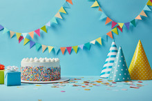 Tasty Cake With Sugar Sprinkles,party Hats And Gifts On Blue Background With Colorful Bunting