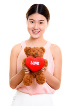 Studio shot of young happy Asian woman smiling and holding teddy