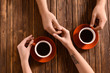 © Pixel-Shot - Young couple with cups of coffee holding hands on wooden table