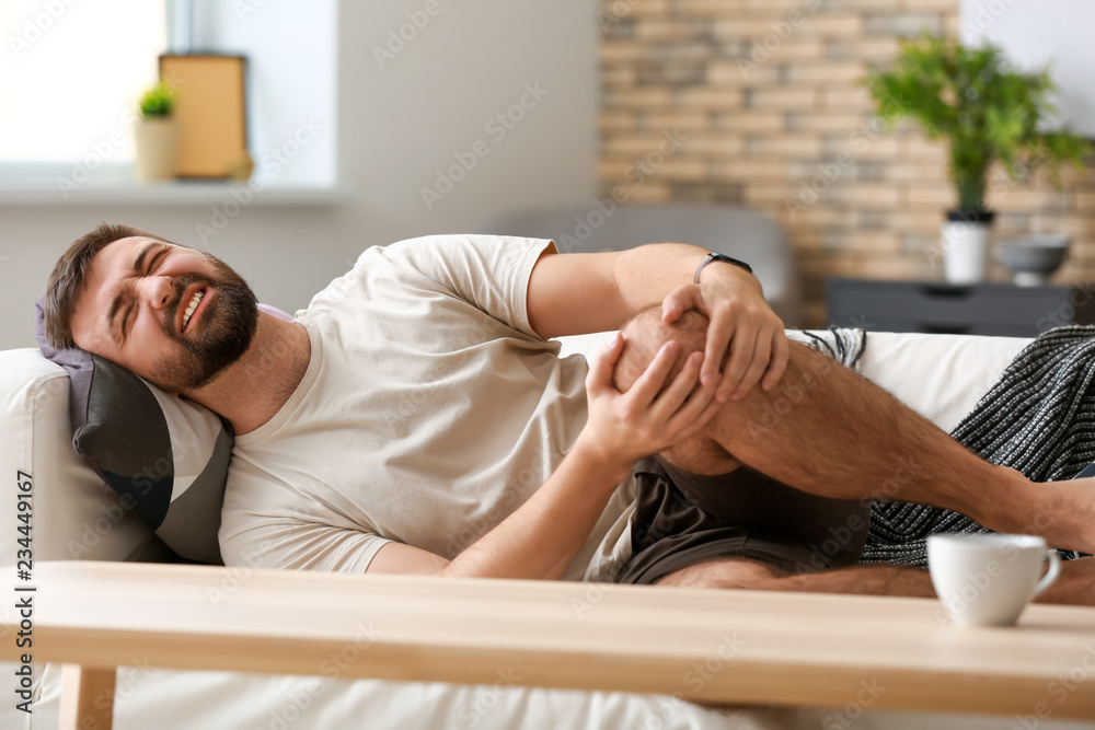 Man suffering from leg pain at home
