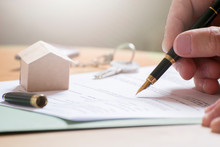 Man Hand Signing Documentation For Home Mortgage With A Pen. Keys And Home Icon With Empty Copy Space For Editor's Text.