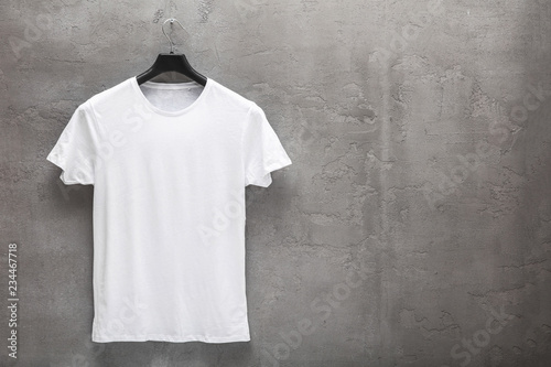 Fotografía Front side of male white cotton t-shirt on a hanger and a concrete wall in the background