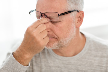 Wall Mural - stress, old age and people concept - close up of senior man in glasses having headache and massaging nose bridge