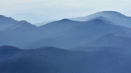 peaceful blue nature background with foggy bucegi mountains in carpathians seen from cota 2000, sina