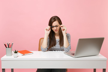 Wall Mural - Exhausted tired woman having problem holding pencil near face sit, work at white desk with contemporary pc laptop isolated on pastel pink background. Achievement business career concept. Copy space.