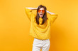 Overjoyed young woman in fur sweater, white pants, heart orange glasses clinging to head, screaming isolated on bright yellow background. People sincere emotions, lifestyle concept. Advertising area.