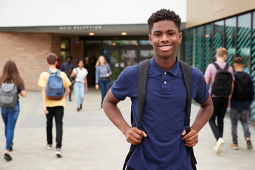 portrait of smiling male high school student outside college building with other teenage students in