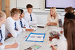 © Monkey Business - Female High School Teacher Sitting At Table With Teenage Pupils Wearing Uniform Teaching Lesson