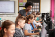 © Monkey Business - Teacher Helping Female Pupil Line Of High School Students Working at Screens In Computer Class