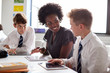 © Monkey Business - Female High School Teacher Sitting At Table With Students Wearing Uniform Using Digital Tablets In Lesson