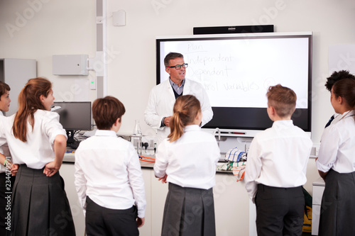 Fotomural Male High School Tutor Teaching High School Students Wearing Uniforms In Science