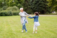 Family, Leisure And People Concept - Happy Grandmother And Granddaughter Playing Game Or Dancing At Summer Park