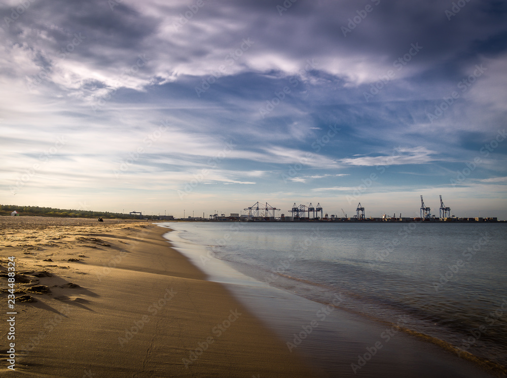 Long empty clean sand Stogi beach in Gdansk, Poland with Stalin shipyard with cranes in the background - obrazy, fototapety, plakaty 