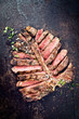 Barbecue dry aged wagyu porterhouse steak sliced and decorated with spice and herbs as top view on an old rusty board with copy space