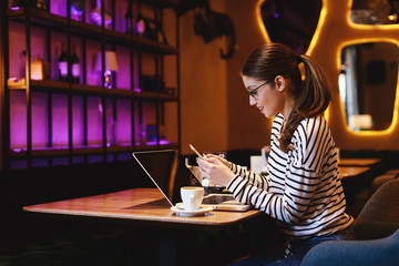 Young woman using smartphone in a cafe with a laptop in front of her