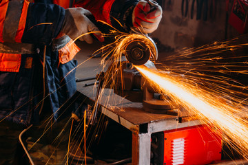 Worker cutting metal with grinder in his workshop. Sparks while grinding iron