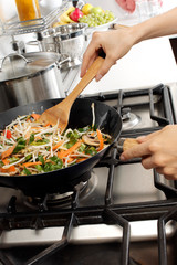 WOMAN IN KITCHEN STIR FRYING VEGETABLES