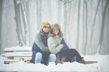 Poster - Young couple with blanket sitting on bench in winter