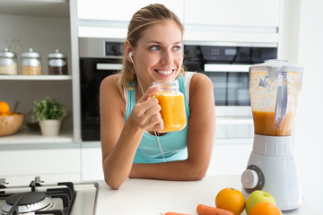 Wall Mural - Beautiful sporty young woman looking sideways and drinking vegetable detox juice in the kitchen at home.