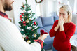 © pressmaster - Young man making proposal to his girlfriend on Christmas eve by decorated firtree