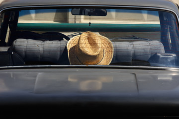 Straw hat in back seat of retro car. Old black automobile close up. Minimalist background with transport of romantic traveler. Vehicle for way in sunny summer day. Copy space. Trip in time vacation.