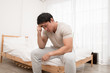 © Asada - Asian man sitting on the bed and hand on forehead. Illness,stress,headache caused by overworking or hard work.