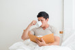 © Asada - Asian Man drinking a cup of coffee or breakfast In bed while reading the book in the morning.