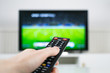 © Michael - Hand holding TV remote control in front of blurred TV background