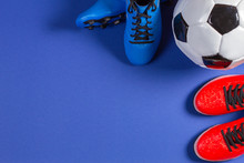 Top View Of Soccer Ball And Two Pairs Of Soccer Football Sports Shoes On Blue Background
