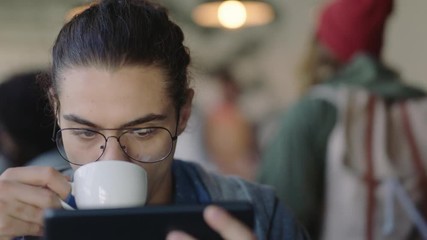 attractive young caucasian man using digital tablet computer in cafe drinking coffee student enjoying watching online entertainment reading social media on portable device wearing glasses
