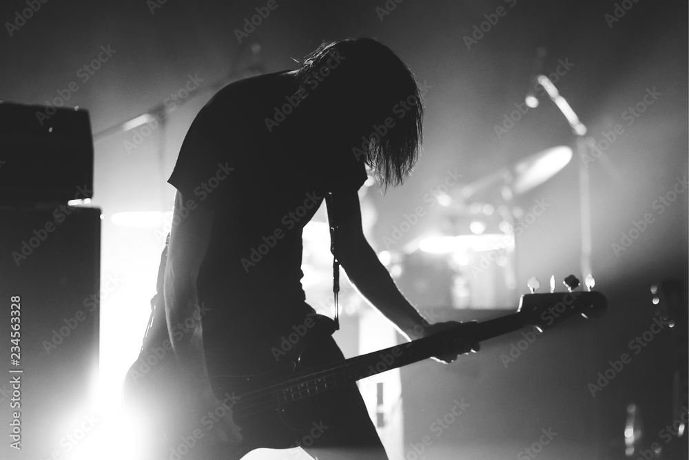 Long hair bass guitarist silhouette on a stage in a backlights playing rock music. Black and white - obrazy, fototapety, plakaty 