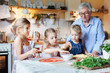 © Mary Anlens - Family and kids cooking pizza in cozy home kitchen. Grandmother and three sisters preparing homemade italian food. Funny little girls helping senior woman, eating ingredients. Children chef concept