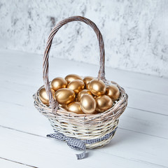 Wall Mural - Easter golden eggs in a wicker basket on white wooden table background