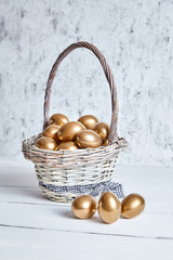 Wall Mural - Easter golden eggs in a basket on white wooden table