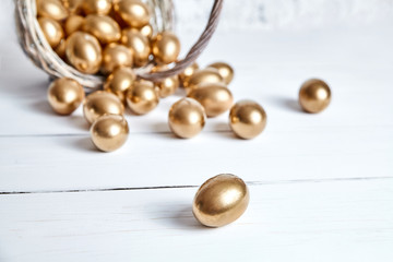 Wall Mural - Easter golden eggs spilled out of wicker basket on white wooden table. Selective focus