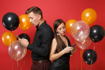 couple stand back to back messaging in cellphone celebrating birthday holiday party isolated on red 