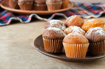 Closeup of a plate with lemon and chocolate muffins on a wooden table, selective focus.