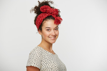 Shot of pretty satisfied young female smiles, rejoices good offer, glad to participate in interesting event, stands sideways, dressed in T-shirt with black polka dots, isolated over white studio wall