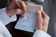 A Doctor Writing A Prescription On A Blue Prescription Pad.
