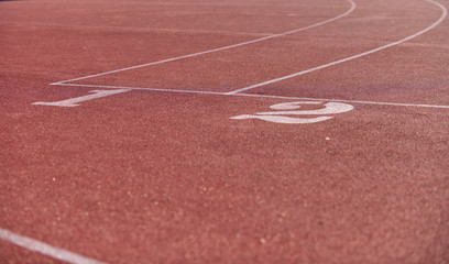 A starting line of brown rubber running tracks with number 1 and 2 painted in a school tracking field during afternoon time ready for athletics to practice.