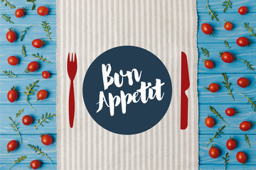 Wall Mural - top view of napkin and cherry tomatoes with arugula on blue table, bon appetit lettering