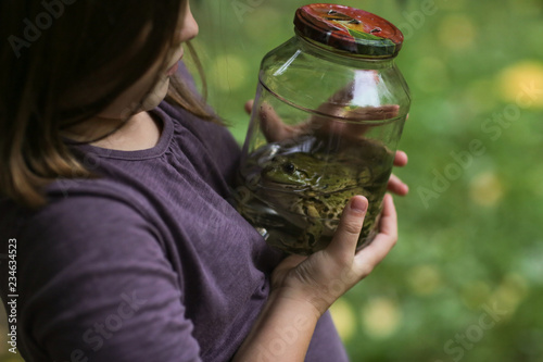Cuadros en Lienzo Child girl holding jar with frog, naturalist