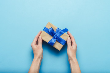 female hands holding a gift with a blue ribbon on a blue background. concept of a gift for the holid