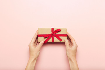 Female hands holding a gift box on a pink background with a question mark. Surprise concept, waiting for a gift for the holidays, birthday, christmas, wedding. Flat lay, top view