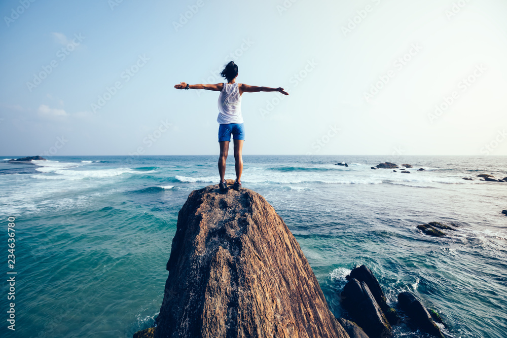 Freedom young woman outstretched arms on seaside rock cliff edge - obrazy, fototapety, plakaty 
