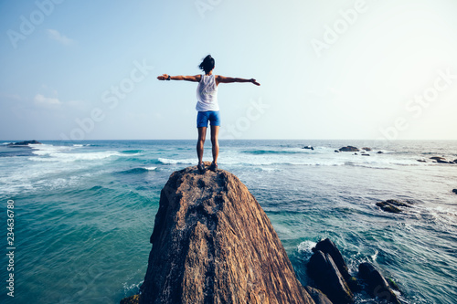 Freedom young woman outstretched arms on seaside rock cliff edge Poster Mural XXL