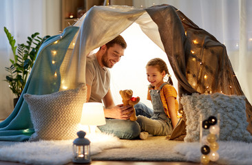 Poster - family, hygge and people concept - happy father with teddy bear toy and little daughter playing in kids tent at night at home